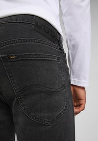 Zwarte denim jeans met een gestructureerde afwerking, opvallende achterzak, gouden logo-detail en een zwarte leren label op de tailleband.