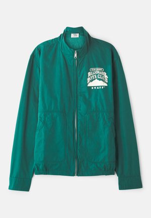 Veste bomber verte avec zip intégral, col montant, deux poches latérales et un imprimé graphique blanc sur la poitrine. Texture de tissu lisse.