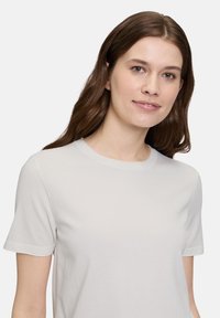 Jasnoszara krótka koszulka z miękkiego materiału, z okrągłym dekoltem, gładką fakturą i prostym designem, bez wzorów czy akcentów.
