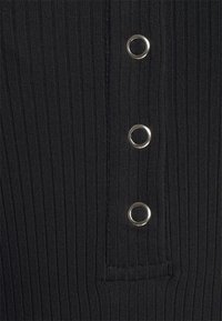 Svart ribbad tyg har tre silverfärgade öglor i en vertikal rad, med en strukturerad yta och sydda kantdetaljer.