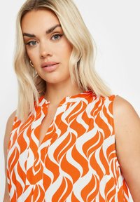 Hihaton paita, jossa on korkea kaulus ja rohkea oranssi-valkoinen liekkikuosi kevyessä kankaassa. Huomaamaton napitusyksityiskohta.