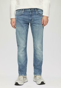 Jeans en denim bleu clair avec une coupe slim, un design à cinq poches et une décoloration subtile. Portés avec des chaussures de sport de teinte neutre.