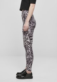Leggings s uzorkom zebre u sivoj i crnoj boji s uskim krojem, s visokim strukom. Nosene s crnim sjajnim cipelama.