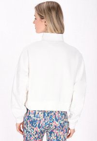 Felpa bianca tagliata con colletto alto, vestibilità rilassata e spalle scese. Abbinata a leggings colorati e fantasia.
