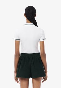 Polo bianco con bordino verde a contrasto, abbinato a pantaloni corti in corduroy verde scuro con vita elastica e vestibilità comoda.