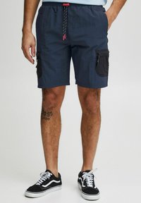 Pantaloni scurți de culoare albastru marin, dintr-un material ușor, cu un brâu elastic, șnur contrastant și buzunare laterale cu detalii din plasă.