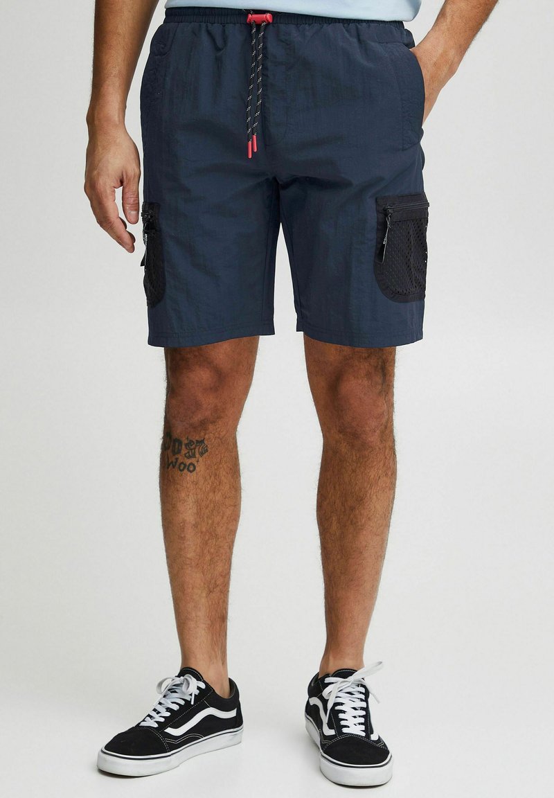 Pantaloni scurți de culoare albastru marin, dintr-un material ușor, cu un brâu elastic, șnur contrastant și buzunare laterale cu detalii din plasă.