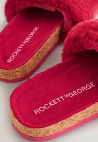 Červené papuče z umelého kožúška s korkovou podrážkou. Majú textúrovaný povrch a svetloružové akcenty. Branding "ROCKETT st GEORGE" je embosovaný vo vnútri.