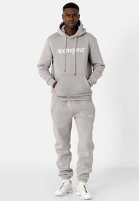 Sweat à capuche en polaire grise avec poche avant, capuche à cordon de serrage et logo à l'avant. Associé à un pantalon de jogging assorti avec poignets élastiques et détail logo.