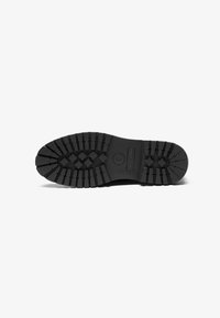 Suela de zapato de goma negra con un patrón de textura y surcos horizontales. Presenta un logo redondo con letras en relieve. Diseño duradero y antideslizante.