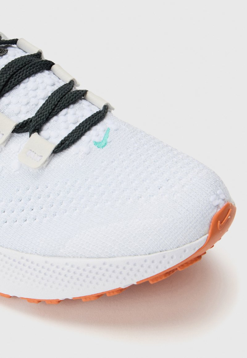 Białe buty sportowe z teksturowaną siateczką, szaro-niebieskimi akcentami, kremowymi sznurówkami i jasnopomarańczową podeszwą.