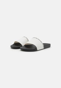 Hvide slidesandaler med en buet strop, sort sål og prægede Calvin Klein-logo. Glat tekstur med en mat finish.