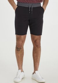 Zwarte katoenen shorts met een grijze elastische tailleband en een trekkoord, voorzien van zijzakken en rafelige zomen, gecombineerd met witte sneakers.