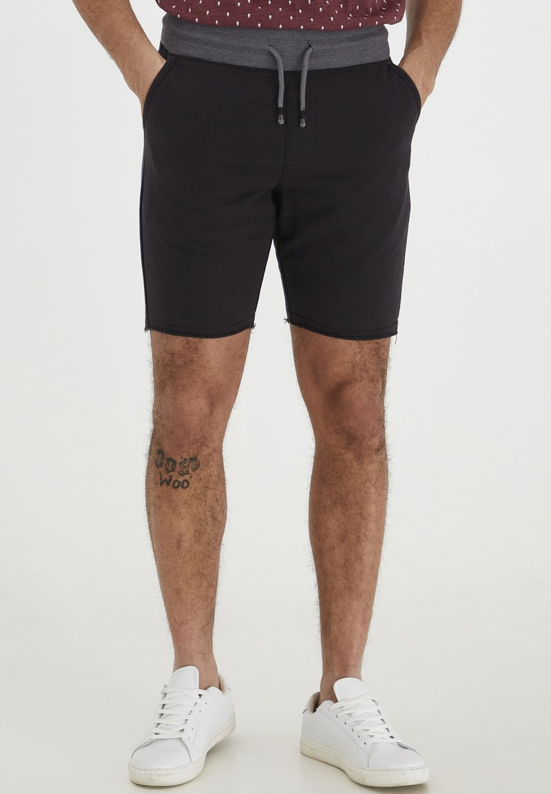 Zwarte katoenen shorts met een grijze elastische tailleband en een trekkoord, voorzien van zijzakken en rafelige zomen, gecombineerd met witte sneakers.
