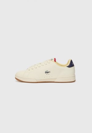 Lacoste sneaker in cream leather with a textured finish. Features a rubber sole, lace-up front, navy heel, and embroidered logo.
