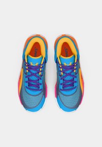 Ζευγάρι πολύχρωμων αθλητικών παπουτσιών με μπλε, κίτρινες, πορτοκαλί και ροζ λεπτομέρειες και μωβ κορδόνια, σε θέα από πάνω πάνω σε λευκό φόντο.
