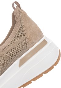 Nahaufnahme der Ferse eines beigen Sneakers aus Strick und Wildleder mit weißer dicker Sohle und hellbrautem Gummi-Profiltreten.