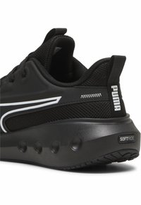 Zwarte sportieve schoen met een gestructureerde mesh bovenkant, zachte rubberen zool met ronde nopjes en witte merkaccenten.