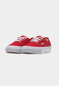Ζευγάρι κόκ κινων καμβά Vans sneakers με λευκά κορδόνια και παχιά λευκή ελαστική σόλα σε απλό ανοιχτόχρωμο φόντο.