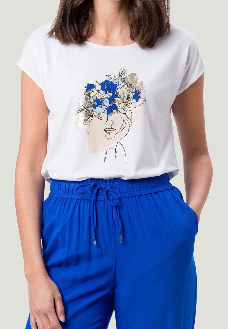 Camiseta blanca con un dibujo lineal de un rostro adornado con acentos florales azules. Combinada con pantalones anchos azules, que muestran un estilo y ajuste relajados.