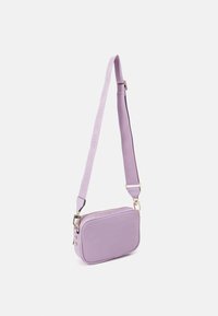 Lila crossbody-väska gjord av mjukt material, med rektangulär form, guldfärgade detaljer och justerbar rem med varumärke.
