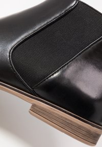 Stivaletto nero in pelle con pannelli laterali elastici, finitura lucida e tacco impilato in legno. Presenta superfici lisce e testurate.