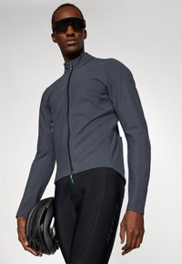 Chaqueta de ciclismo gris para hombre con cuello alto, cremallera completa y acentos turquesa. Pantalones cortos de ciclismo negros ajustados con inserto acolchado y logo.