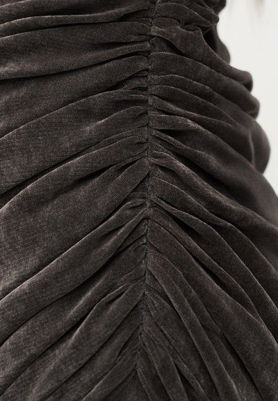 Κοντινό πλάνο σκούρου γκρι υφάσματος με συγκεντρωμένη, ρυτιδωτή υφή που σχηματίζει συμμετρικές κάθετες πτυχές.