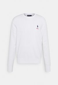 Vit långärmad sweatshirt i bomull med ribbad halsringning och ärmslut. Har en liten blå logotyp och röd text "Polo" på bröstet.