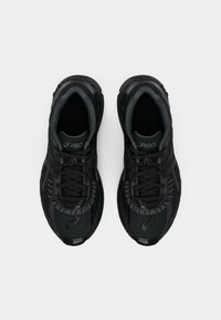 Chaussures de sport noires avec une tige en mesh, des accents texturés, un laçage et une semelle rembourrée. Logo affiché sur la languette.