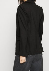 Czarna marynarka o dopasowanym kroju, z miękkiej tkaniny, z długimi rękawami i subtelnymi klapami z wcięciem; posiada pojedyncze rozcięcie z tyłu i brak widocznych elementów metalowych.