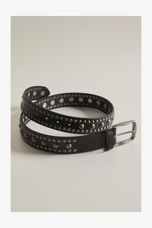 Cinturón de cuero negro con tachuelas metálicas plateadas en patrones circulares y una hebilla rectangular plateada, enrollado sobre una superficie clara.