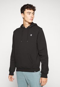 Sort hættetrøje lavet af blødt stof, med en front kangaroo lomme, snore og et lille hvidt logo på brystet.