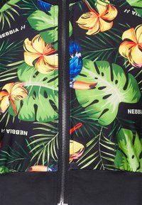 Kukkakuosiset vetoketjulliset takki mustalla alaosalla; sisältää värikkäitä trooppisia kuvioita lehdistä ja kukista, sileää kangasta sekä erottuvan vetoketjun.
