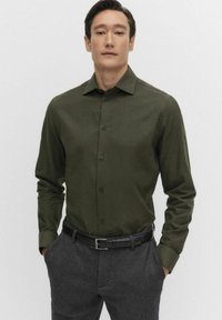 Musta vihreä pitkähihainen napillinen paita sileästä kankaasta, jossa on terävä kaulus ja etupaneeli. Yhdistetty harmaisiin housuihin ja mustaan vyöhön.