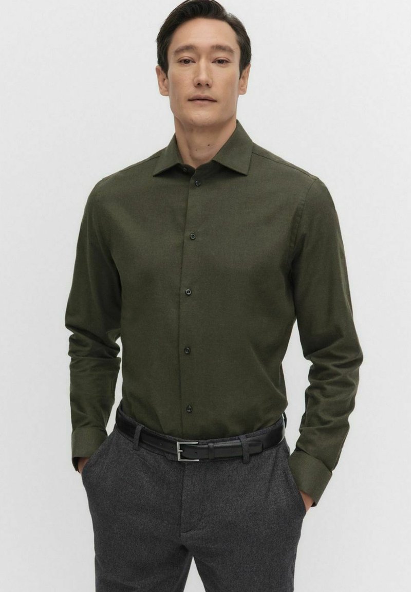 Musta vihreä pitkähihainen napillinen paita sileästä kankaasta, jossa on terävä kaulus ja etupaneeli. Yhdistetty harmaisiin housuihin ja mustaan vyöhön.