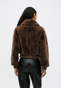 Brązowa kurtka z sztucznego futra w wzór chevron, z szerokim kołnierzem i ściągaczami. Połączona z czarnymi skórzanymi spodniami z wysokim stanem.