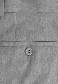 Tessuto grigio e strutturato con una cucitura orizzontale e un bottone a quattro fori al centro. Un motivo sottile aggiunge profondità al materiale.