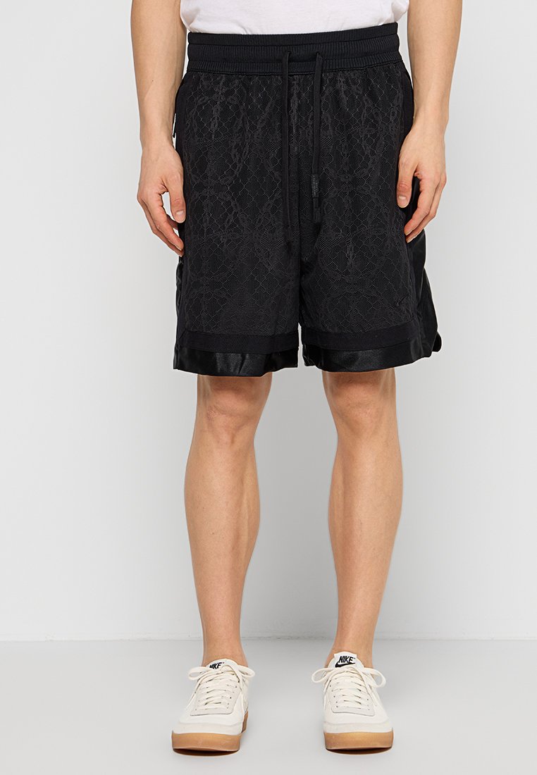 Shorts de sport noirs en tissu texturé, avec une taille élastique et un bord en satin noir au niveau de l'ourlet. Poches plates sur les côtés.