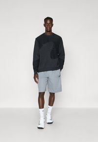 Black sweatshirt with an abstract design, paired with gray shorts; features white Nike branding on the shorts and shoes. White socks and athletic shoes.