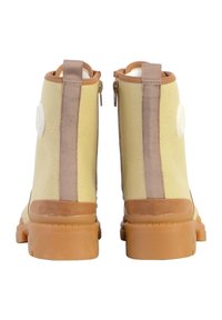 Gele canvas enkellaarsjes met bruine rubberen zolen, voorzien van een achterrits en contrasterende zijstrepen. Witte logo-detail op de hiel.