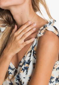 Bluzka w kwiaty z dekoltem w serek, zdobiona niebieskimi i żółtymi kwiatami na białym tle. Związania na ramieniu, lekki materiał.