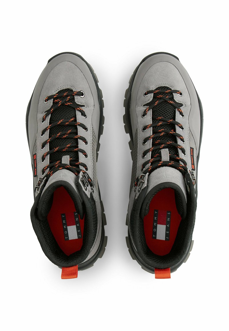 Graue Wanderschuhe mit schwarzen Akzenten, strukturierter Oberfläche, orangen Schnürsenkeln und rotem Innenfutter. Sie verfügen über Gummisohlen und Markenetiketten an den Seiten.