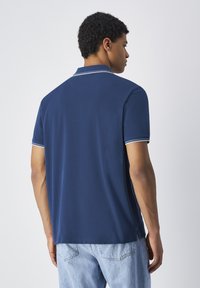 Granatowa koszulka polo o prostym wzorze, z płaskim kołnierzem i białymi paskami na kołnierzu oraz rękawach. Miękka tkanina.