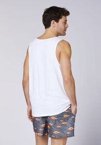 Weißes Tanktop mit lockerem Sitz, kombiniert mit grauen Shorts, die ein oranges Känguru-Muster aufweisen. Der Stoff wirkt leicht und glatt.