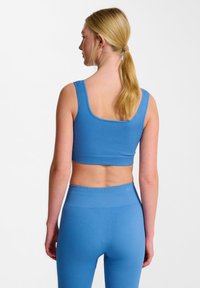 Niebieski prążkowany crop top z szerokimi ramiączkami, połączony z dopasowanymi legginsami o wysokim stanie. Tekstura jest gładka z delikatnymi pionowymi liniami.