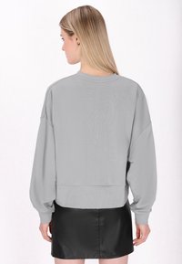 Felpa grigia oversize con maniche lunghe e larghe e orlo a coste, abbinata a una minigonna nera. Tessuto morbido e design casual.
