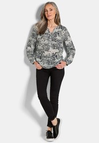 Langärmlige Bluse aus leichtem Stoff mit einem schwarz-weißen abstrakten Muster, kombiniert mit schwarzen Skinny-Jeans und schwarzen Sneakers.