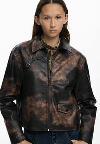 Smeđi i crni jakna od umjetne kože s okovratnikom, prednjim zatvaračem i džepom s lijeve strane. Materijal ima teksturirani, mrljasti uzorak.