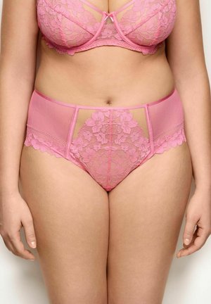 Mujer con sujetador de encaje rosa y braguitas de encaje a juego de talle alto, mostrando el torso delantero y las piernas superiores sobre un fondo neutro.